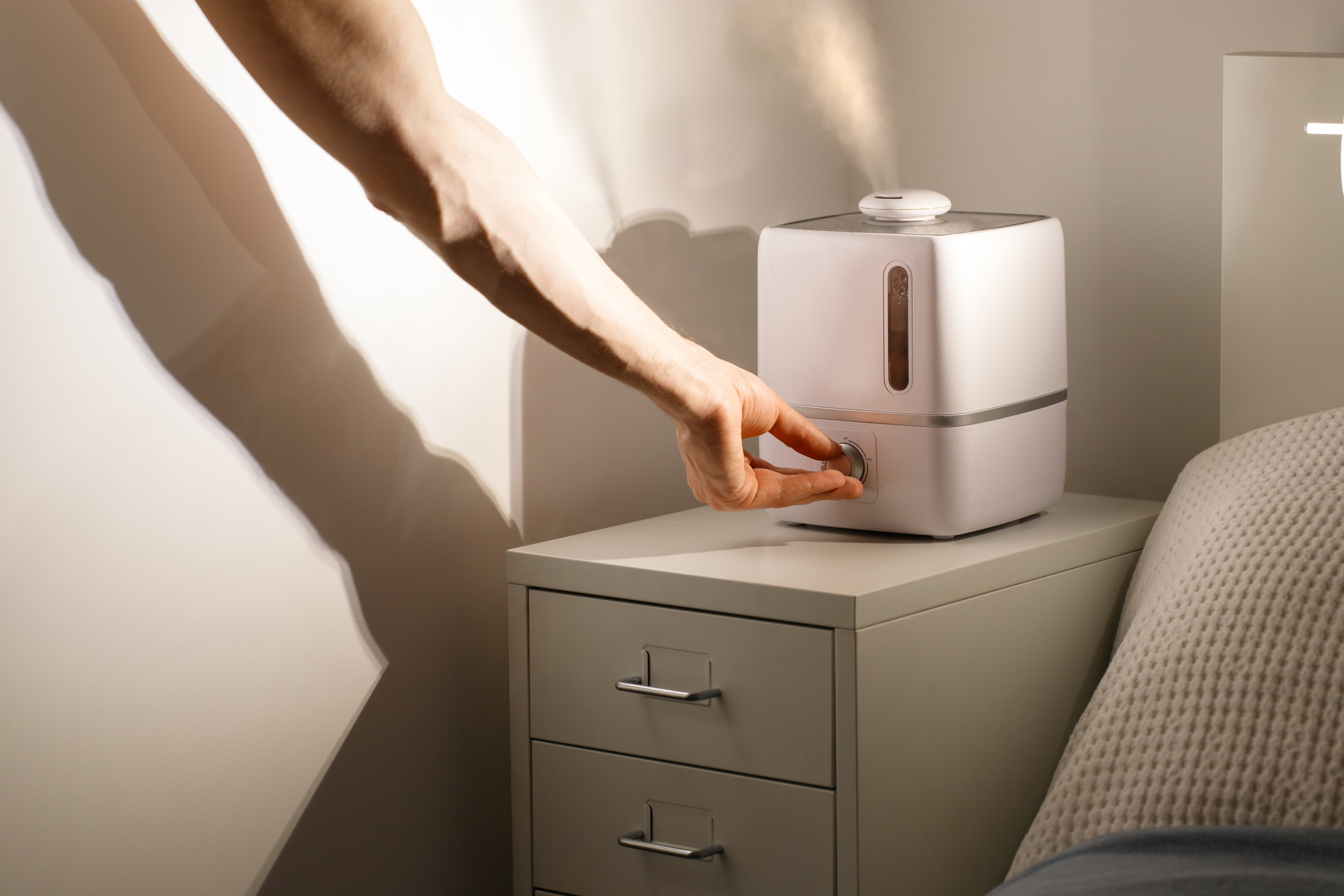 An image of a hand turning on a humidifer in the bedroom. 