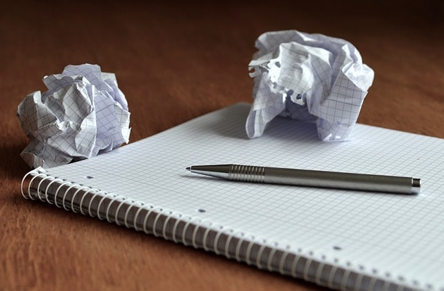 A notebook with a pencil on it surrounded by crumpled paper.