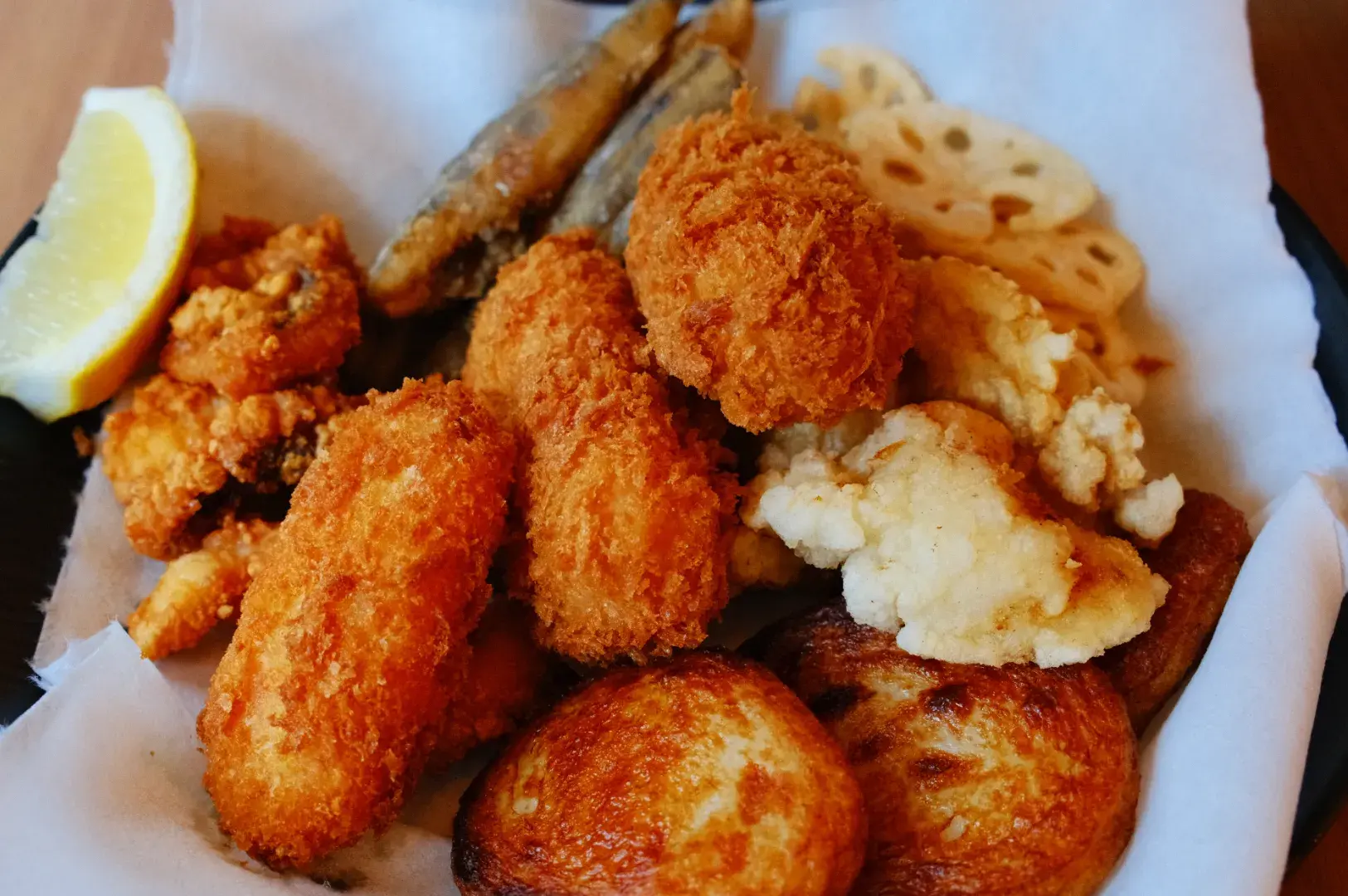 A plate of fried food including golden-brown breaded pieces, fried fish, and slices of lotus root, garnished with a lemon wedge.