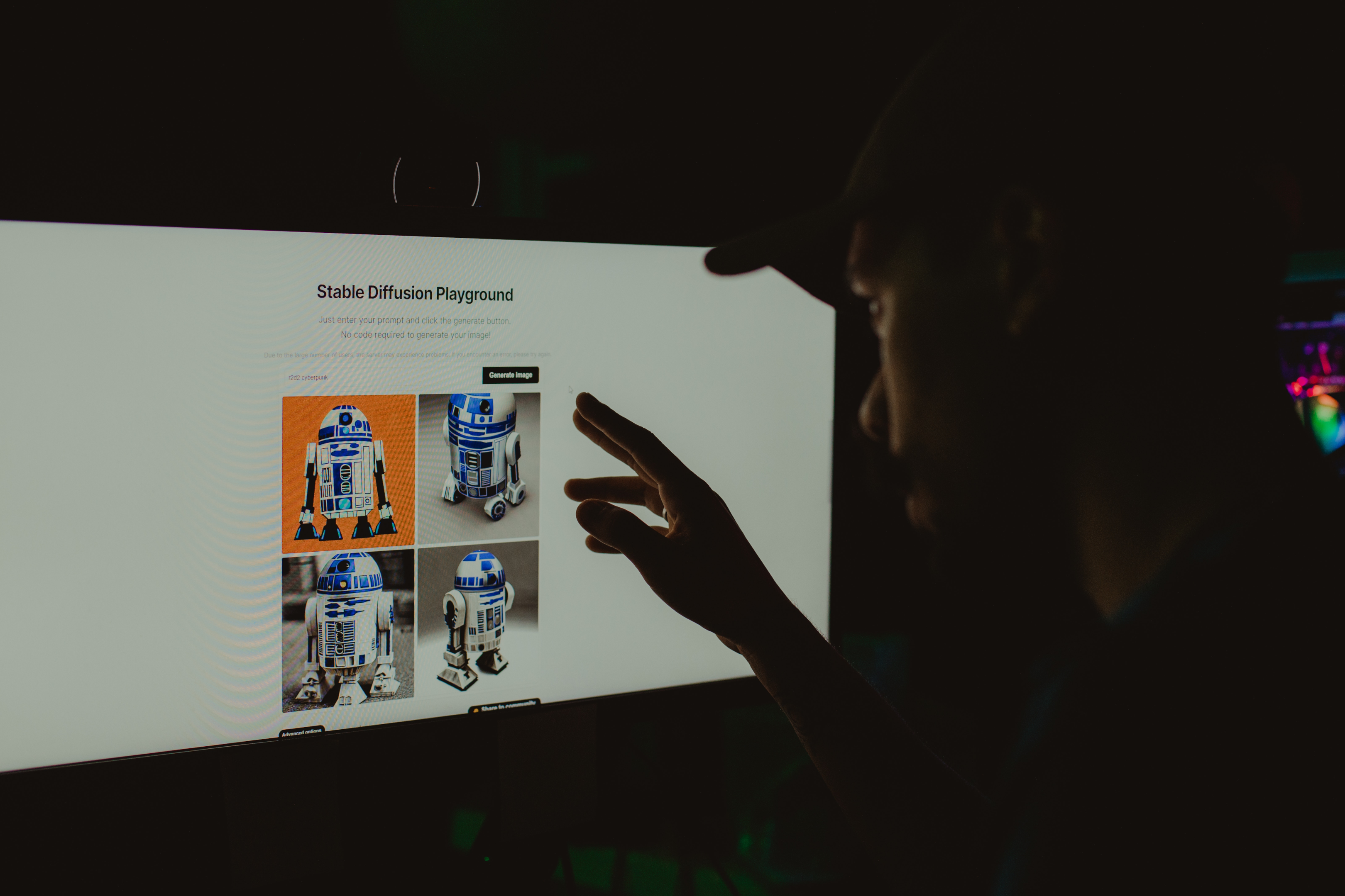 A man looking at the computer screen. The screen shows a page titled: Stable Diffusion Playground, and 4 pictures of a robot resembling R2-D2.