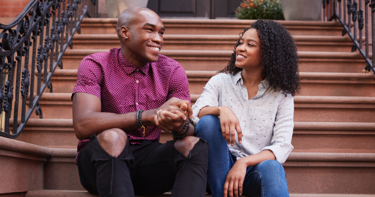 An image of a couple smiling and holding hands on a stoop in New York City, symbolizing the potential for healthier and happier relationships through couples therapy at Loving at Your Best Marriage and Couples Counseling.