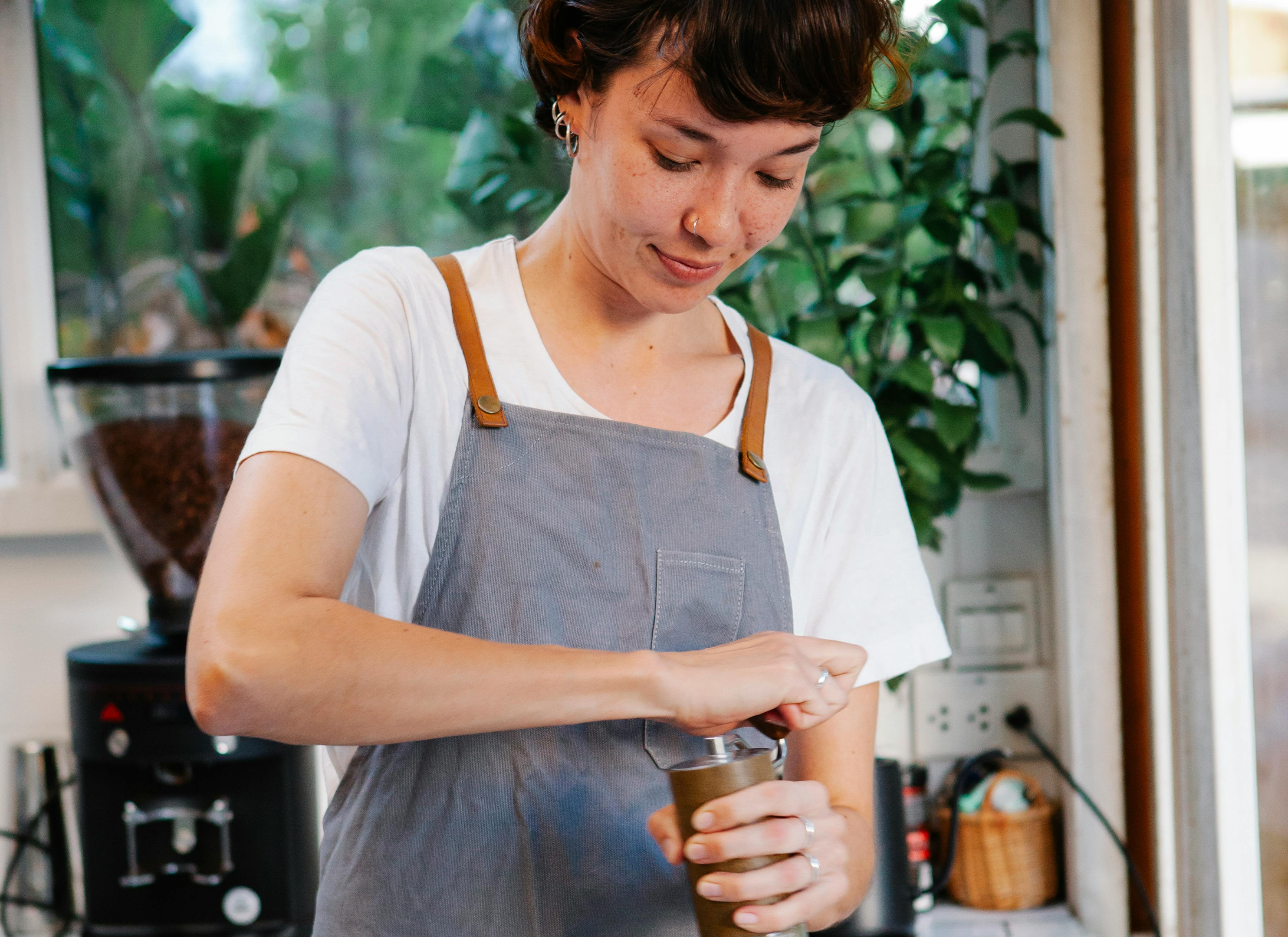 female barista operating a manual coffee grinder