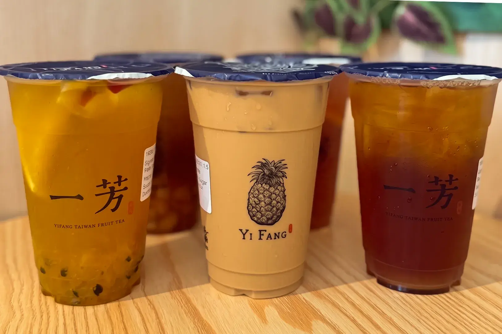 Group of plastic takeaway cups filled with various Yi Fang Taiwan Fruit Tea beverages, featuring a prominent pineapple logo cup in the center.