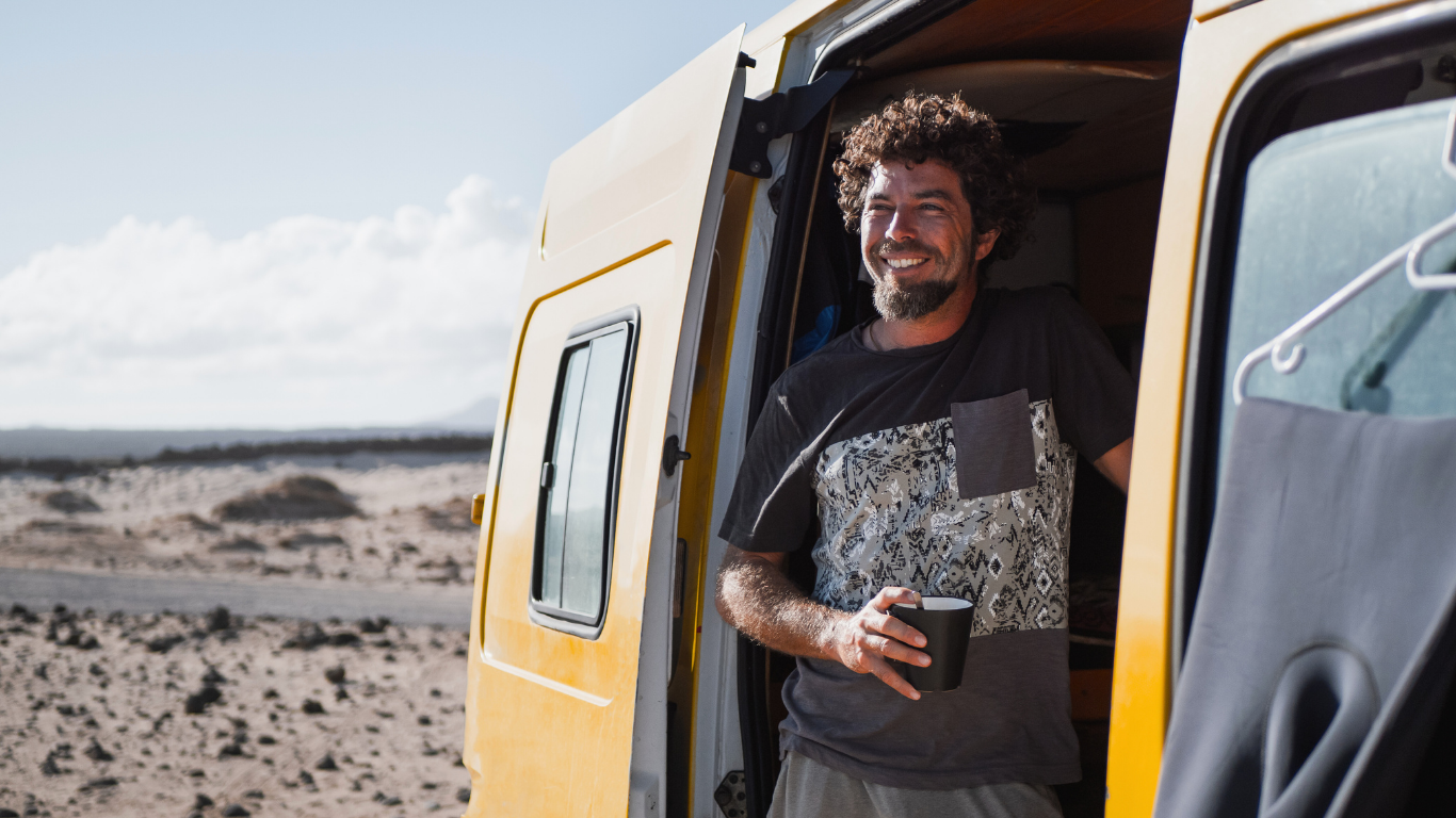 Lächelnder Mann mit Kaffeebecher steht an der offenen Tür eines orangen Campers