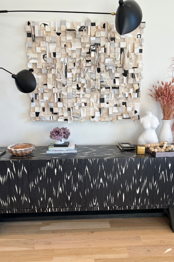 a contemporary artwork in neutral tones hanging above a black sideboard with decor objects on top