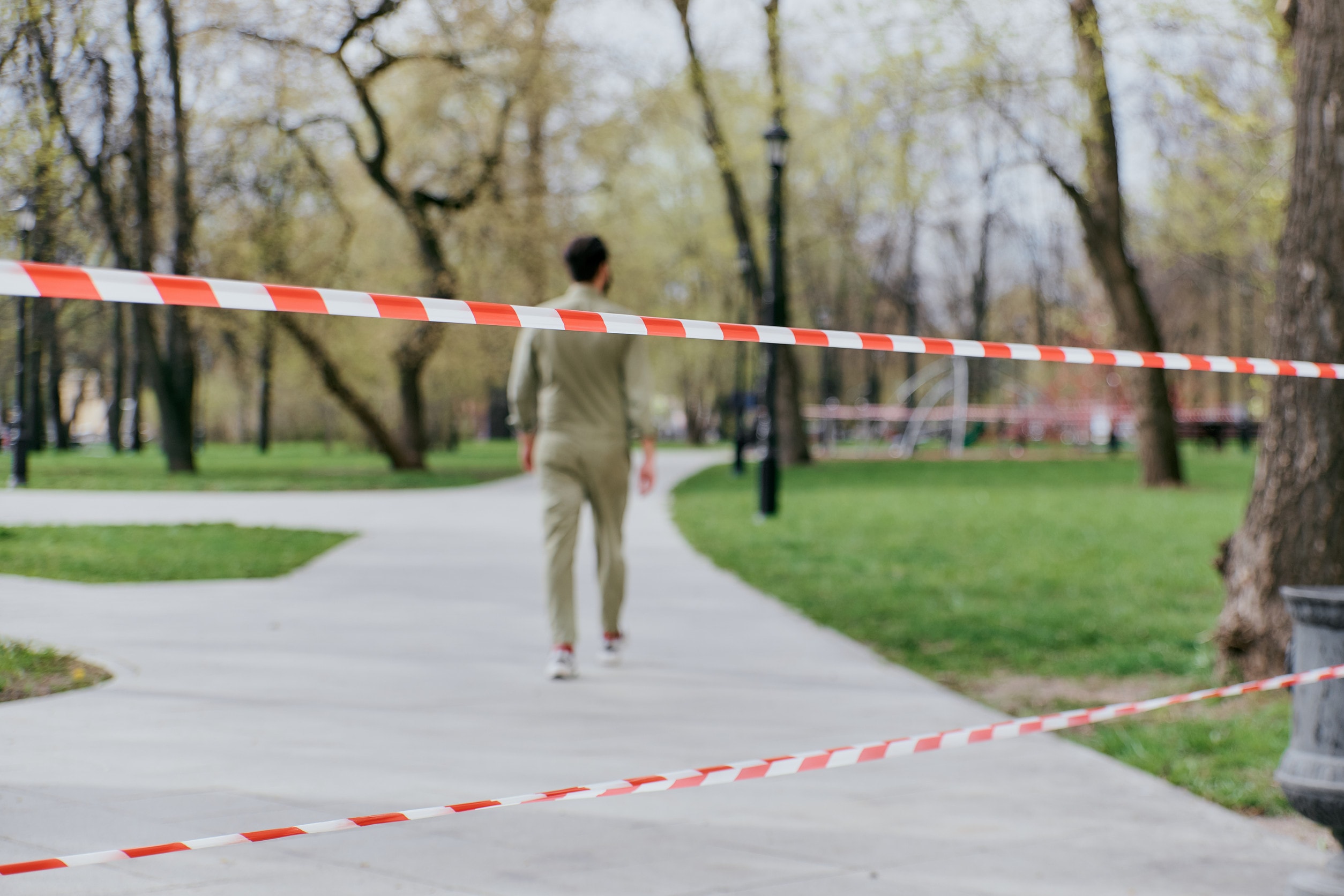 A man walking behind caution tape put up by local authorities after an accident in a public park