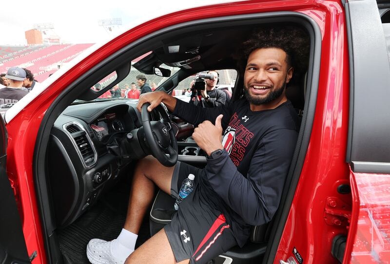 Smiling Utah football player sitting in a new red truck, giving a thumbs-up after receiving an NIL-sponsored vehicle.