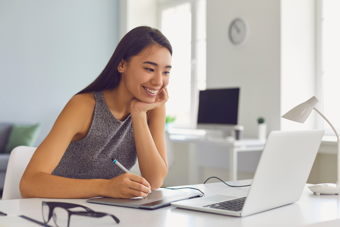 Young Filipino woman smiling at her laptop while being onboarded remotely, showing signs of inclusion and engagement