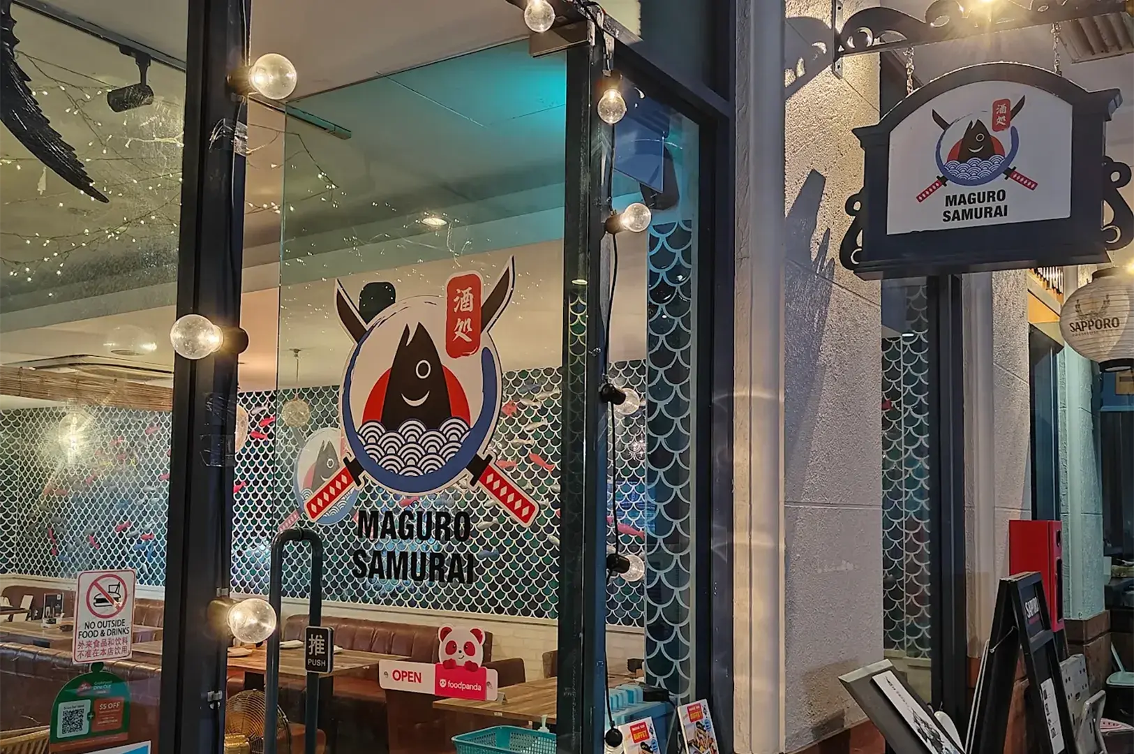 Glass entrance door and hanging signboard of Maguro Samurai restaurant featuring its samurai tuna fish logo.