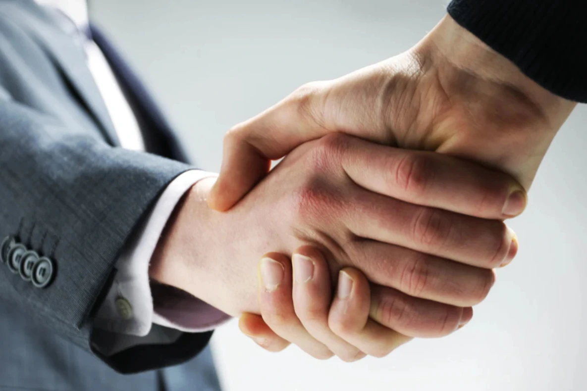 Two people shaking hands after a deal, one wearing a suit.