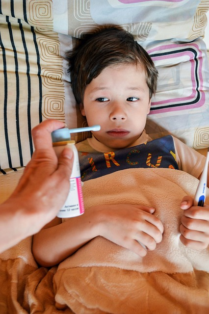 An image of a hand holding a bottle of throat spray to a little boy who is sick in bed. 