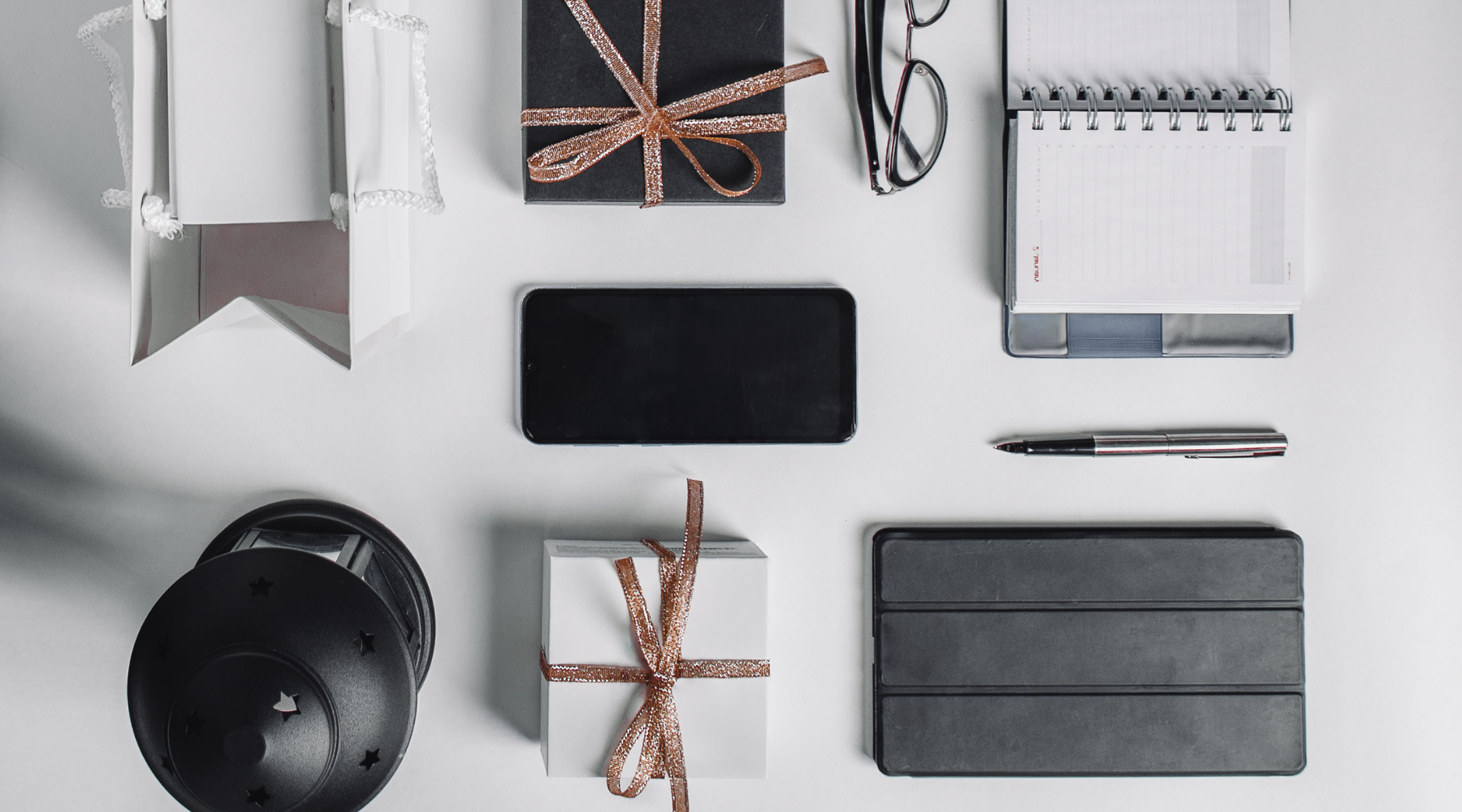 Top view of a minimalist desk setup with gift bags, a notebook, and modern gadgets.