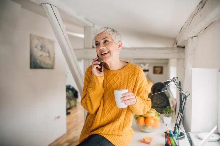 Cheerful blonde woman in an orange sweater having coffee and talking on her cell.