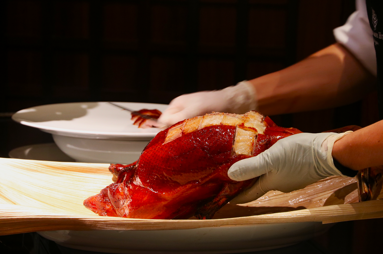 Gloved hands expertly carve a glistening roasted duck on a wooden board. A white plate is ready in the background, emphasizing a culinary presentation.