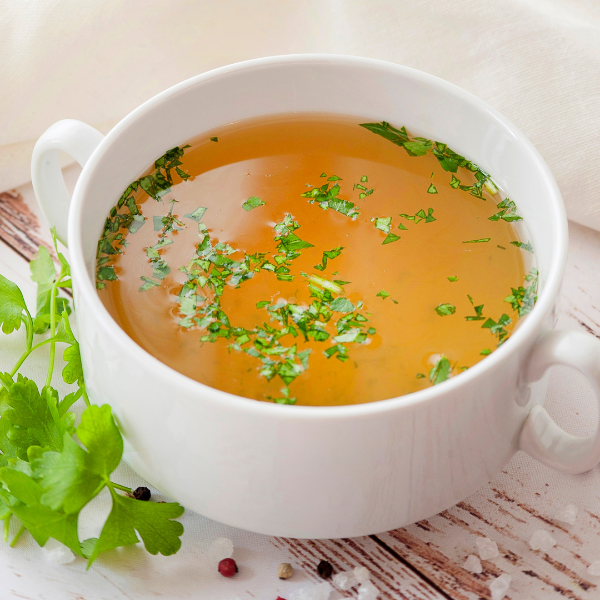 An image showing a bowl of bone broth with fresh herbs.