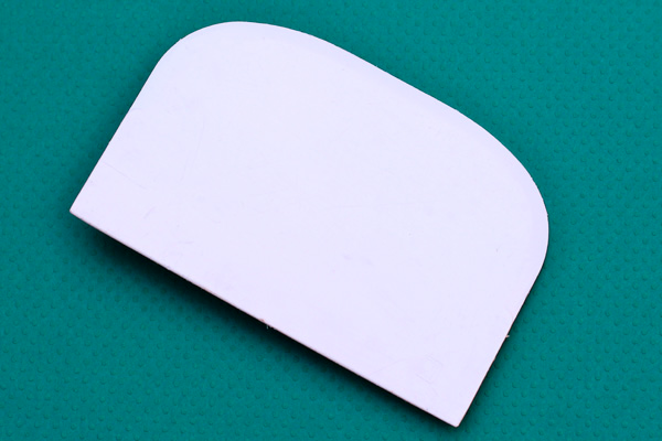 white plastic bench scraper on teal background