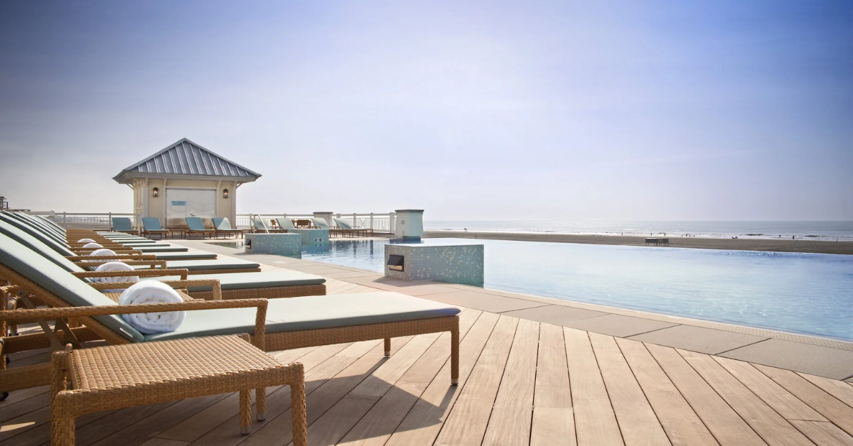 Luxurious oceanfront infinity pool lined with lounge chairs and a cabana, overlooking the beach and ocean.