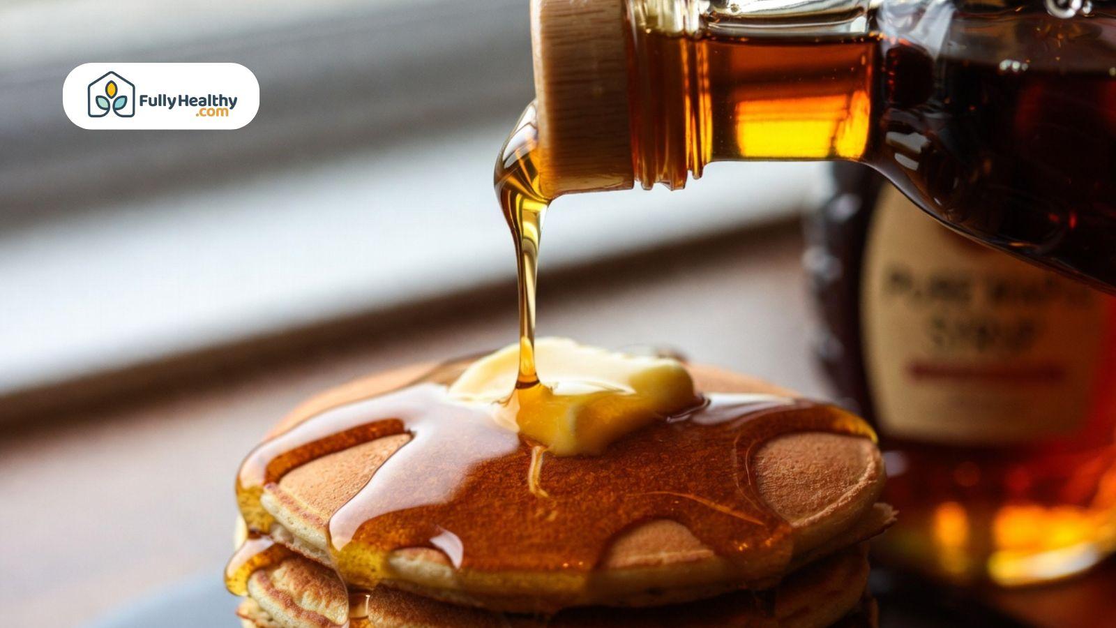 Maple syrup pouring over fluffy pancakes with melting butter in a cozy breakfast setting.