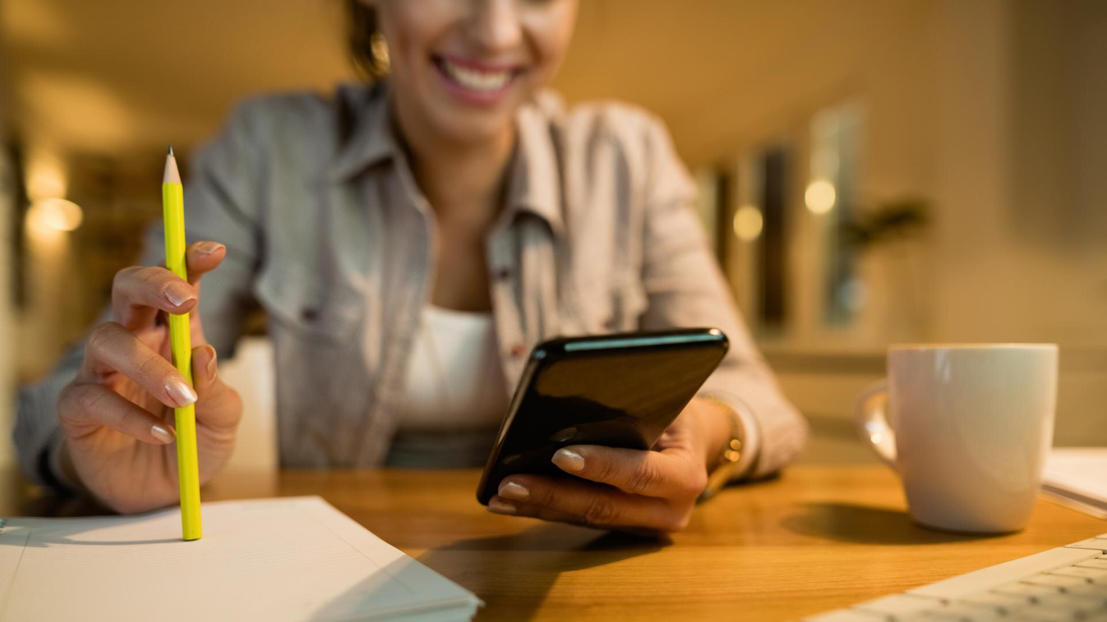 Smiling woman using a smartphone while working, showing how VoIP increases efficiency and enables cost-effective communication.