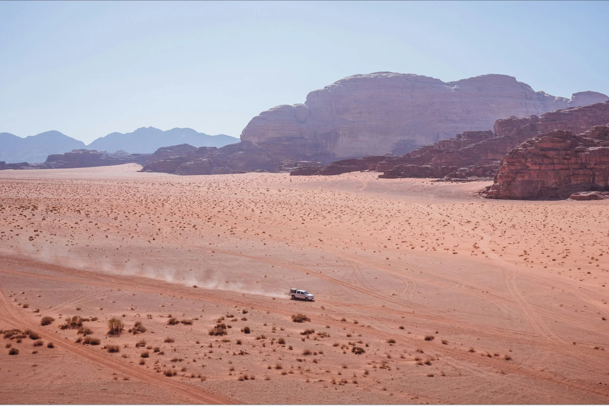 White Land Rover drives off-road in red desert with large rock formations