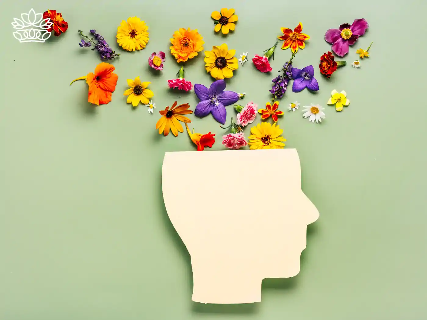 Creative representation of a human head silhouette surrounded by a vibrant array of colorful flowers on a green background, symbolizing mental well-being and harmony included in mental health gift boxes from Fabulous Flowers and Gifts. Delivered with thoughtful attention and care.