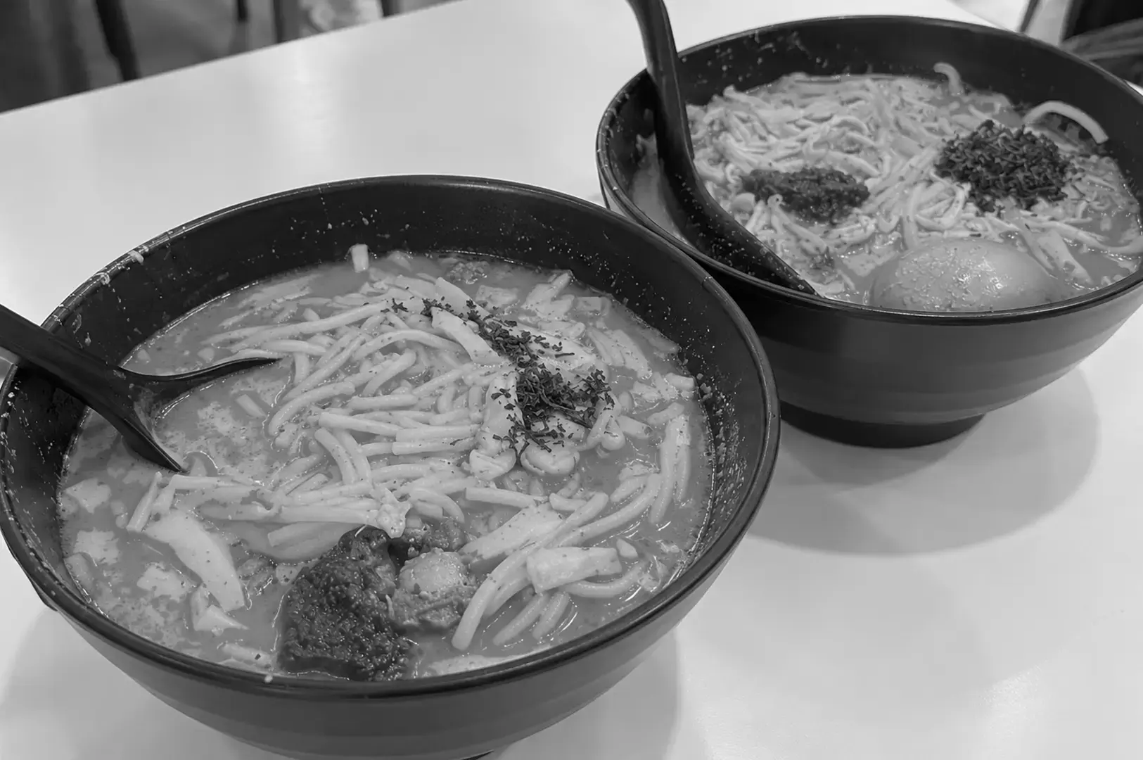 A bowl of laksa noodles soaking in creamy broth, topped with herbs and served at a Singapore hawker eatery.