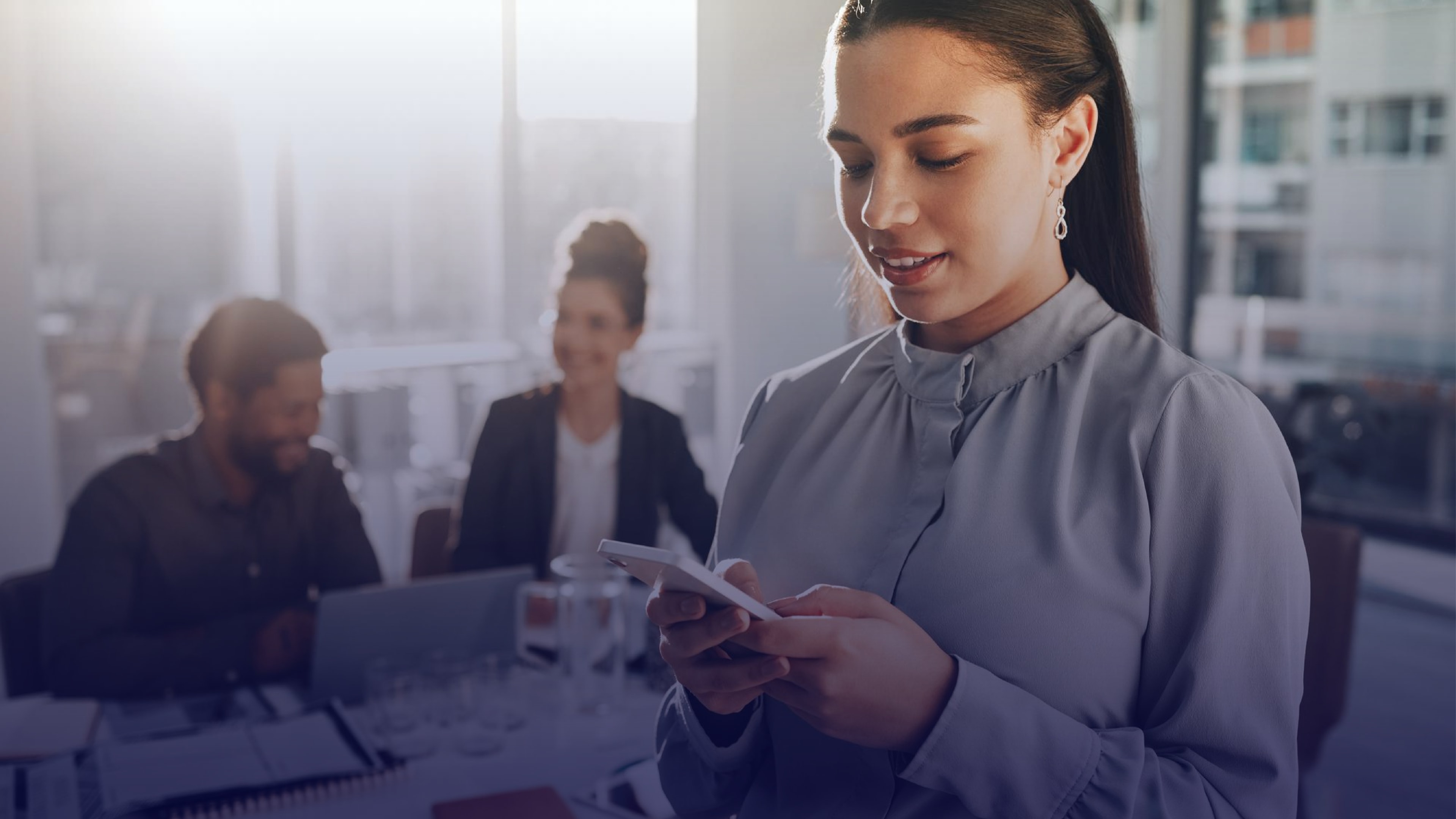 Professional woman checking a mobile alert with colleagues in the background, illustrating internal communications during critical events.