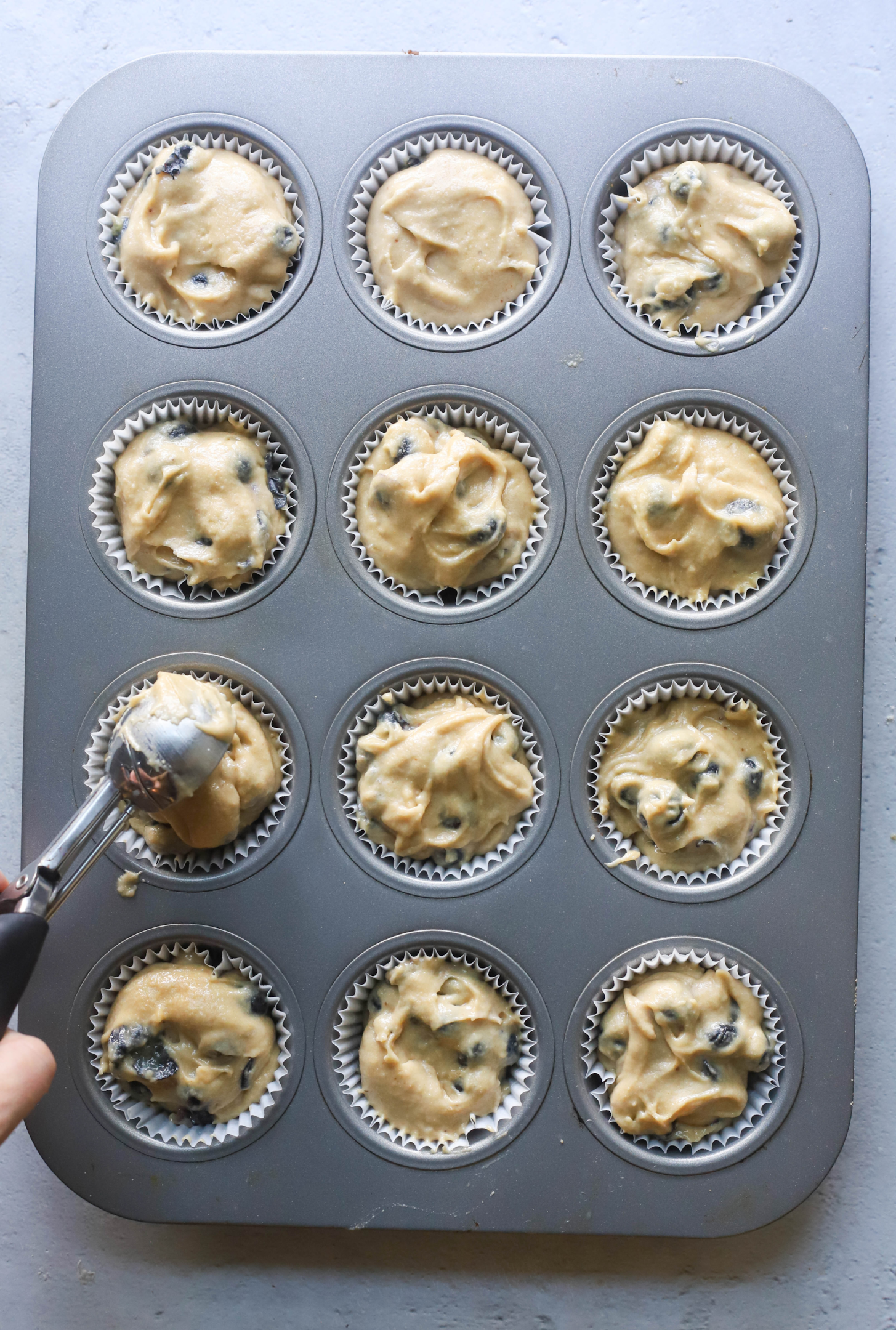 muffin batter being scooped into a muffin tin with a large scoop