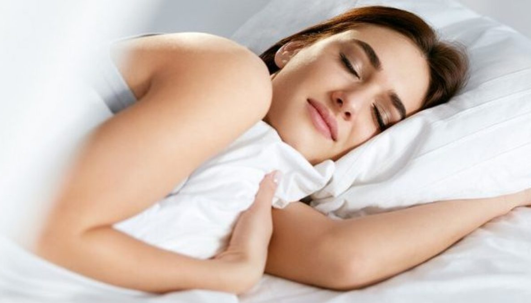 Snorkeskinne: Liten Skinne, Stor Effekt på Søvnen 21 Kvinne sover fredelig på siden med et mildt smil, og holder et hvitt putevar tett inntil seg i en lys seng.