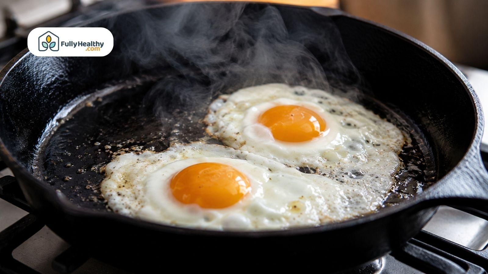 Two fried eggs cooking in a black skillet with steam rising.