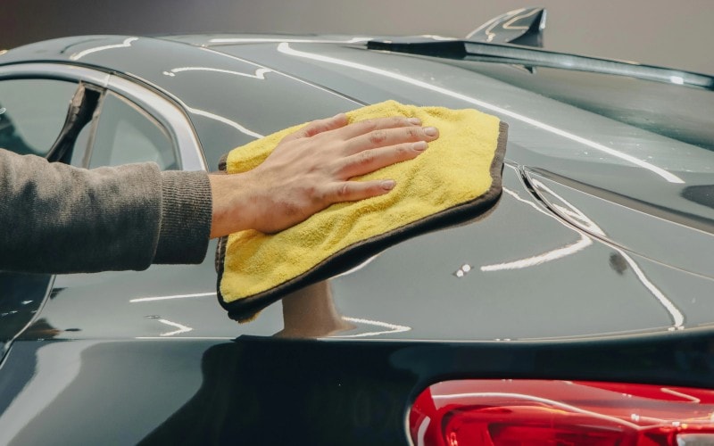A person waxing a car with a microfiber cloth.