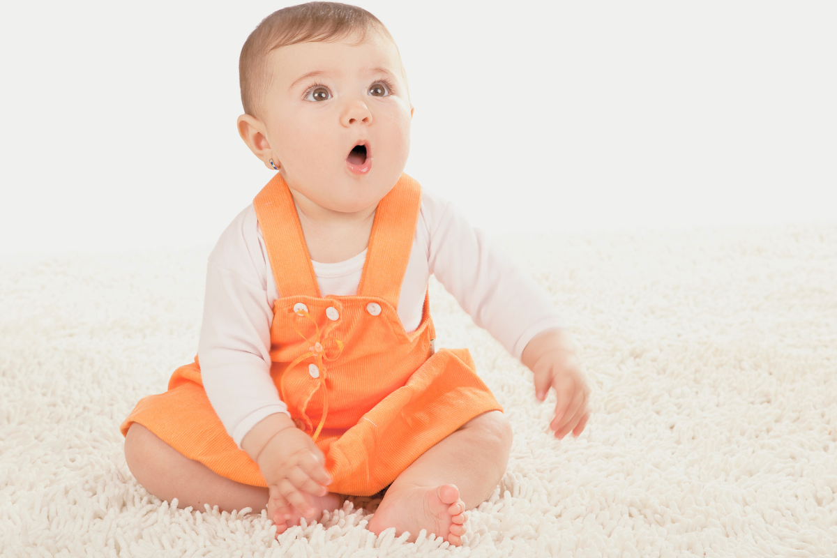 Baby girl sitting on rug. Poppyseed Play