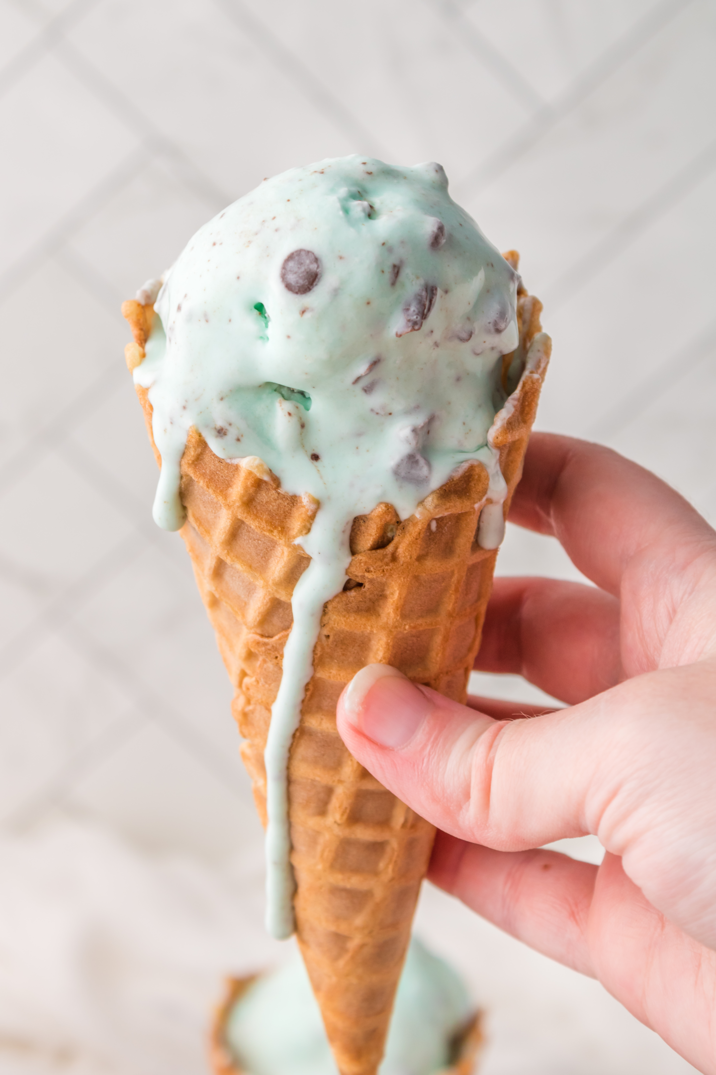 hand holding ice cream cone with scoop of mint chocolate chip ice cream