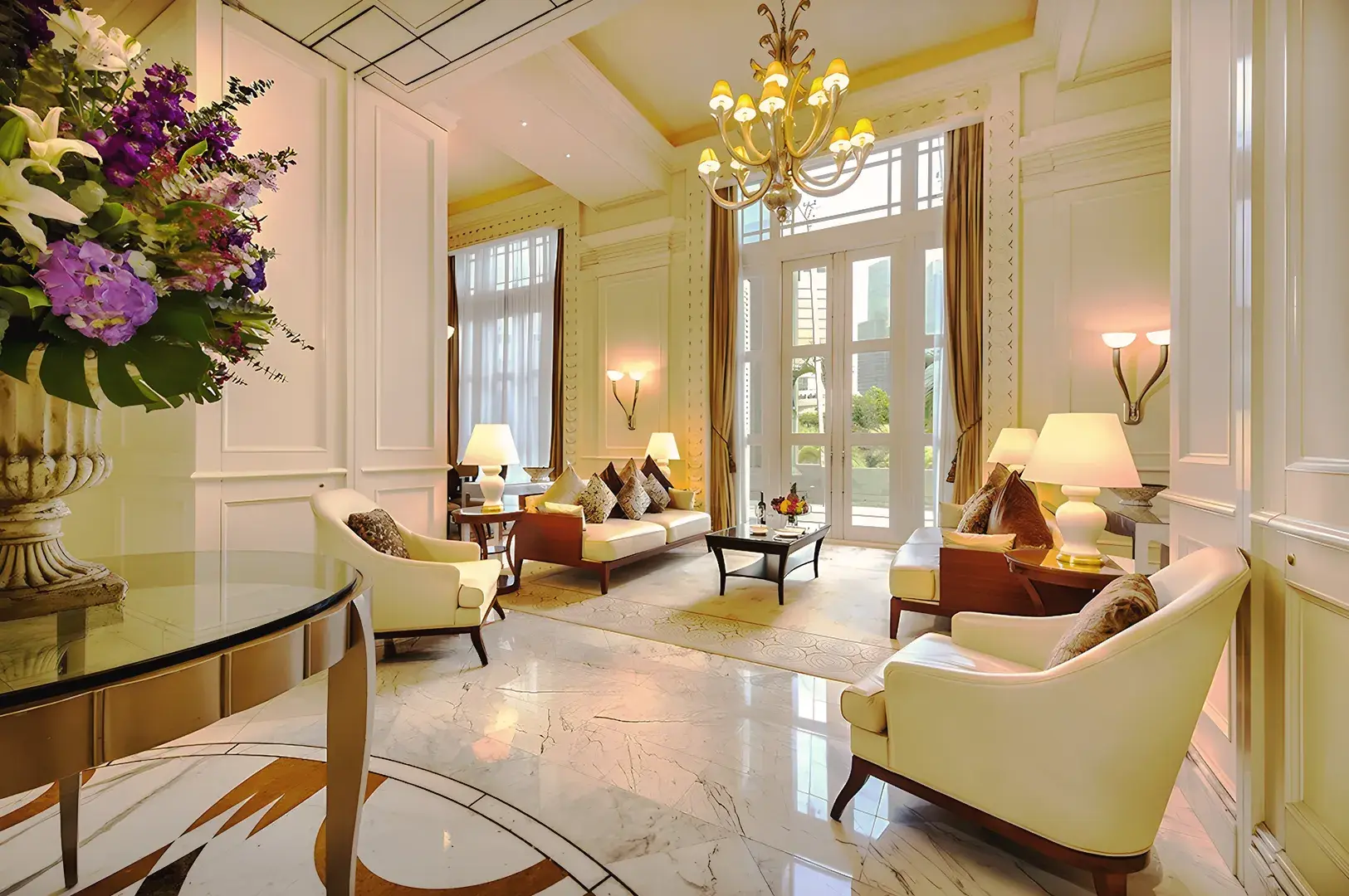 Luxurious Fullerton Hotel lounge in Singapore with marble floors, chandeliers, and classic cream furnishings.