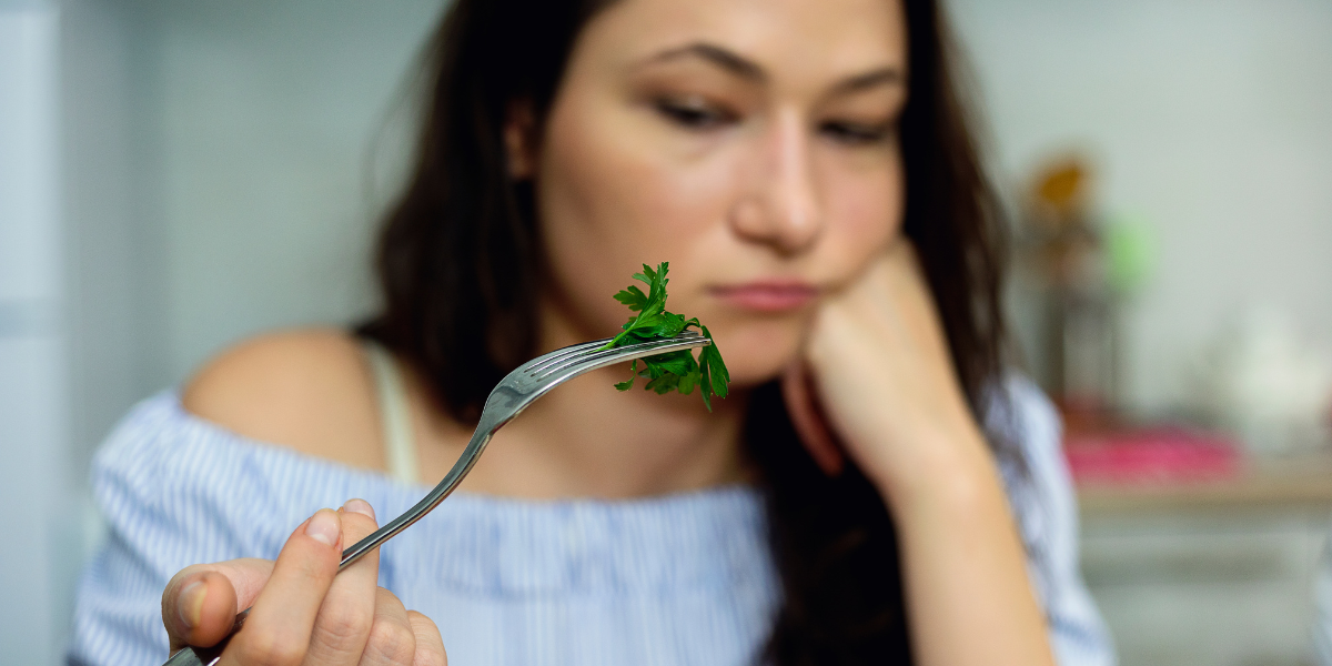 Reverse dieting can be hard if you're not hungry. Image of soman looking sadly at a fork with fresh parsley on it.