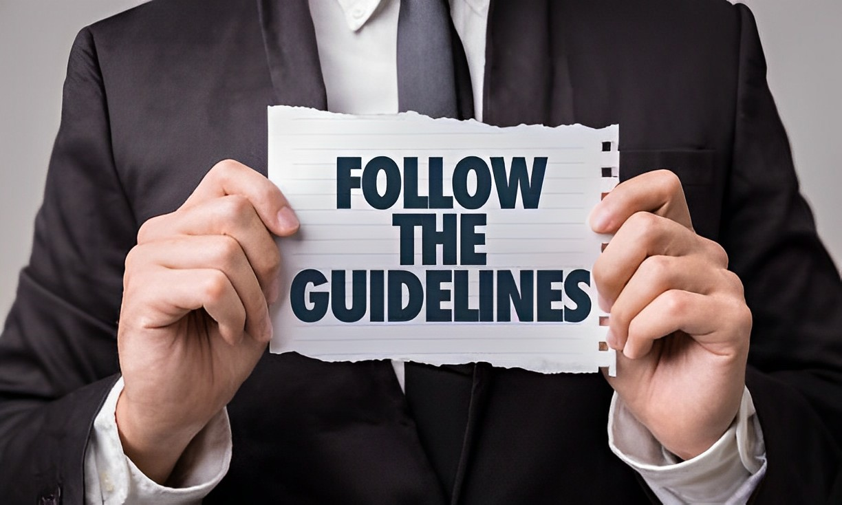 A photo of a well-dressed man holding a paper with FOLLOW THE GUIDELINES written on it
