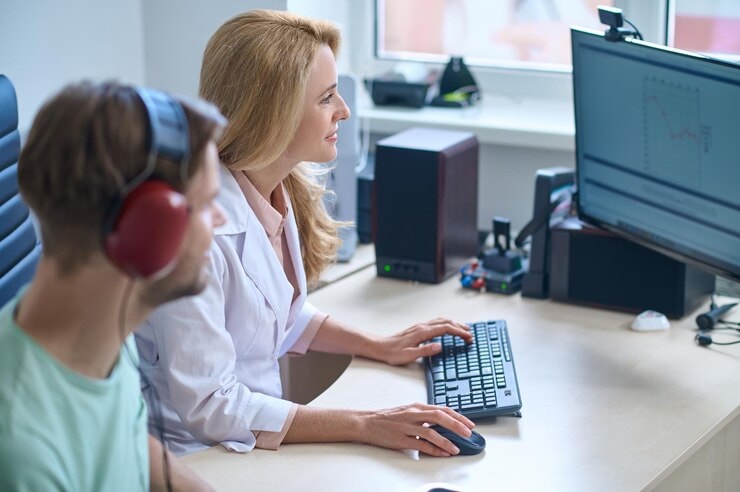 Audoiologist in front of a computer discussing hearing test results with a male patient