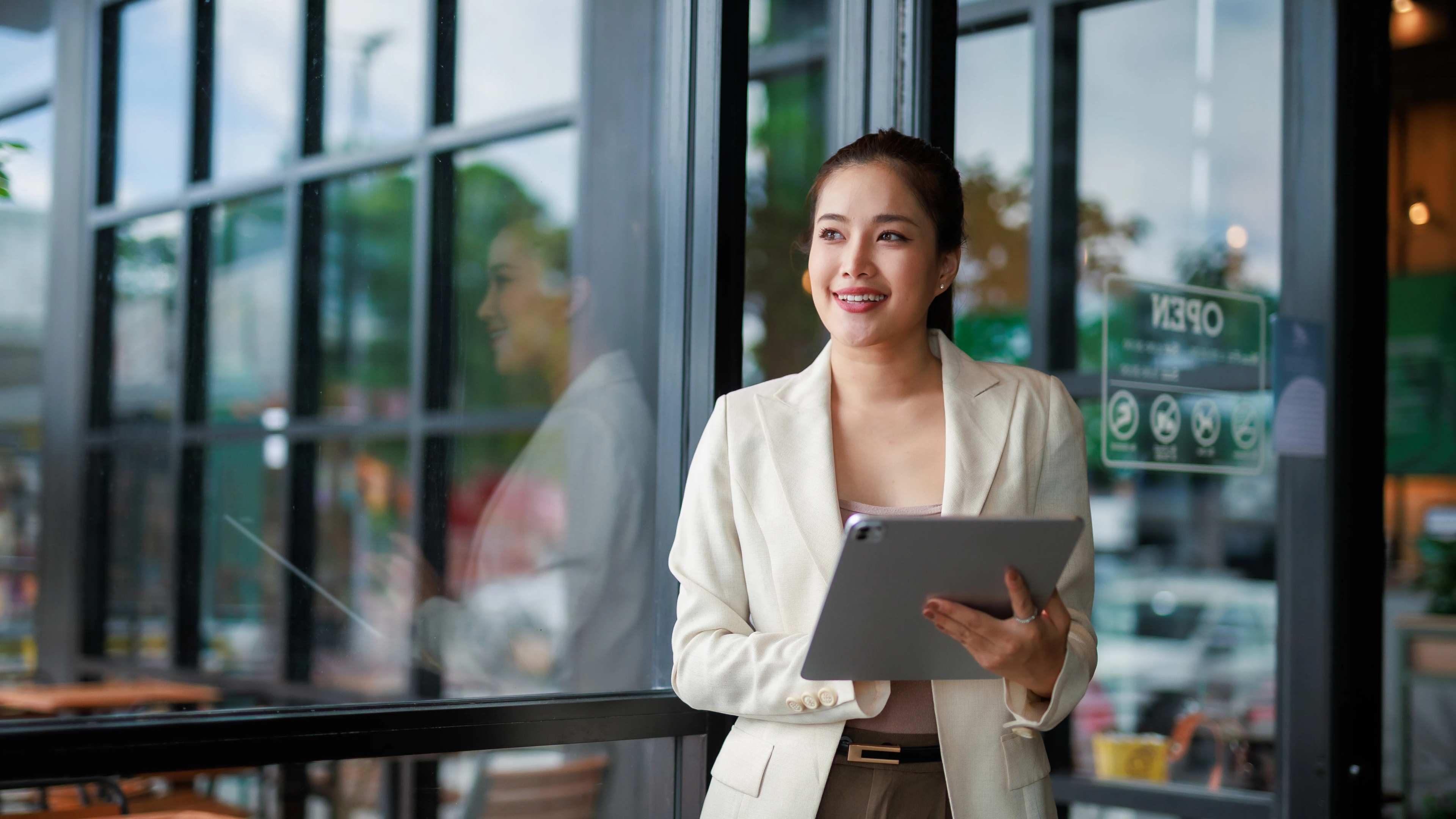 Bbusiness owner standing outside her shop with a tablet, planning future growth and scalability for a small business website through SEO and digital marketing.