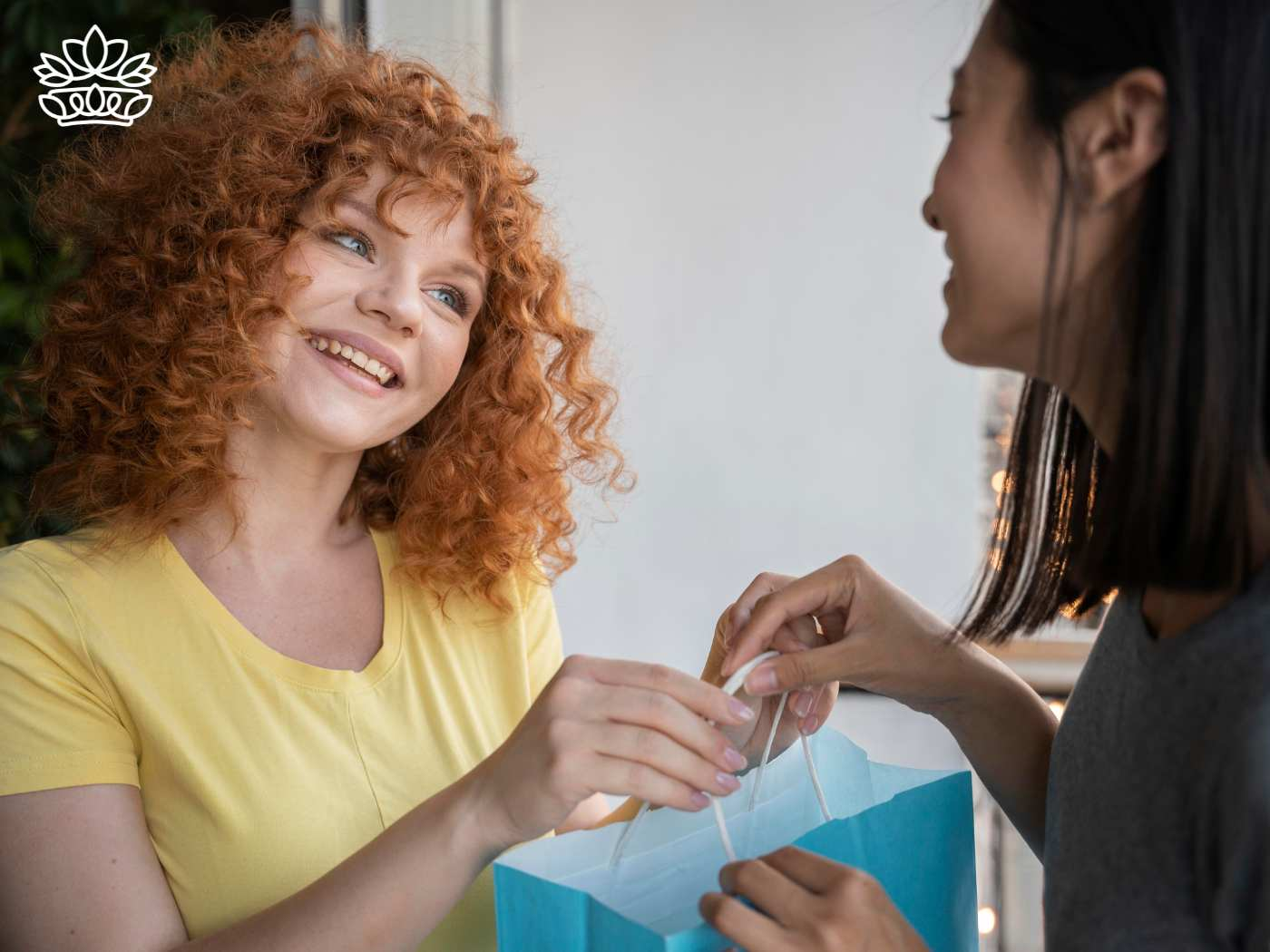 oyful woman with curly red hair receiving a gift box from a friend, expressing happiness and gratitude, from the Gift Boxes by Type Collection at Fabulous Flowers and Gifts.