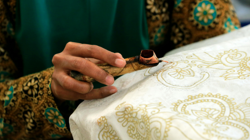 A person is waxing a piece of batik fabric on a table.
