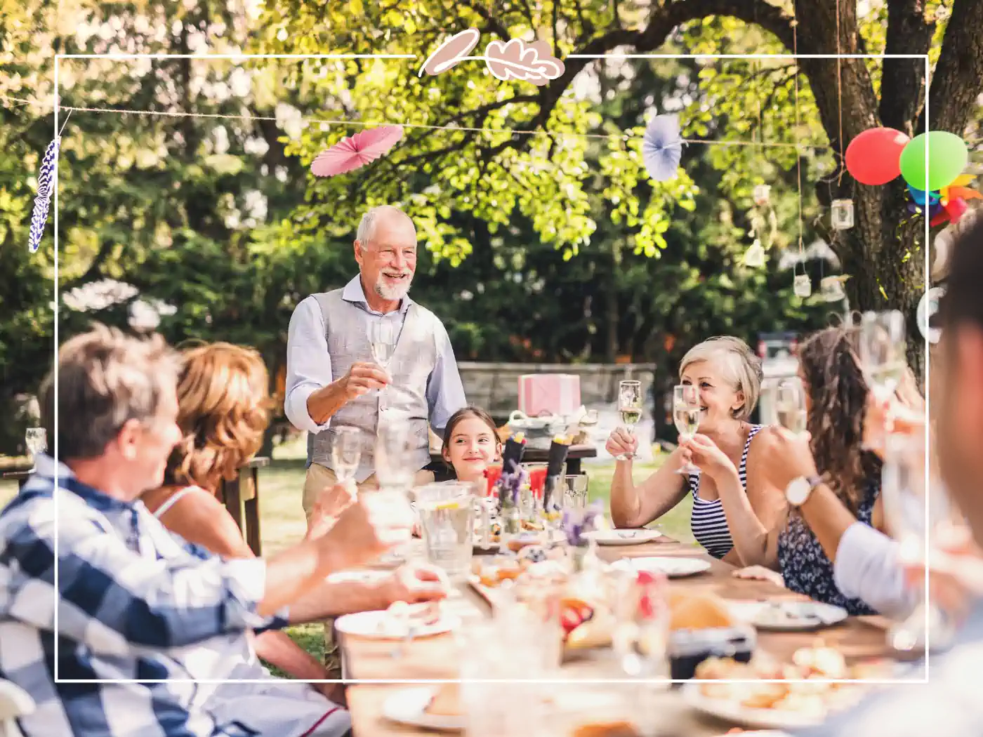 An outdoor family gathering with adults and children seated around a table, celebrating with food and drinks. Fabulous Flowers and Gifts - Birthday Collection.