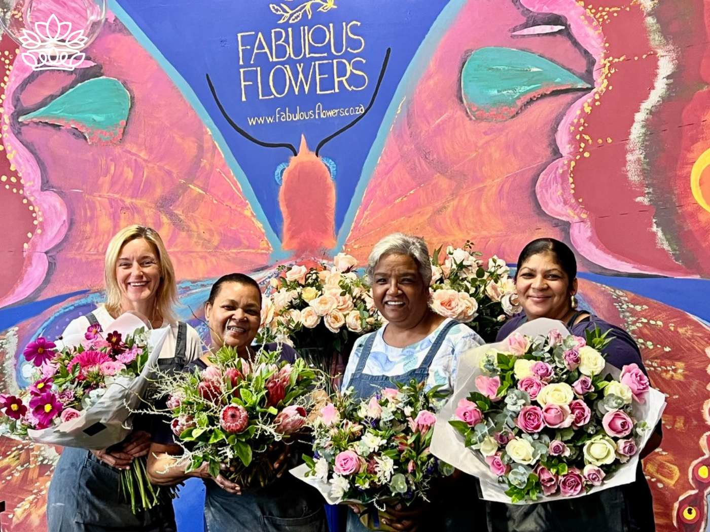 Four cheerful florists holding vibrant bouquets of flowers, with the Fabulous Flowers and Gifts logo proudly displayed in the background, showcasing their artistry and passion for floral arrangements.