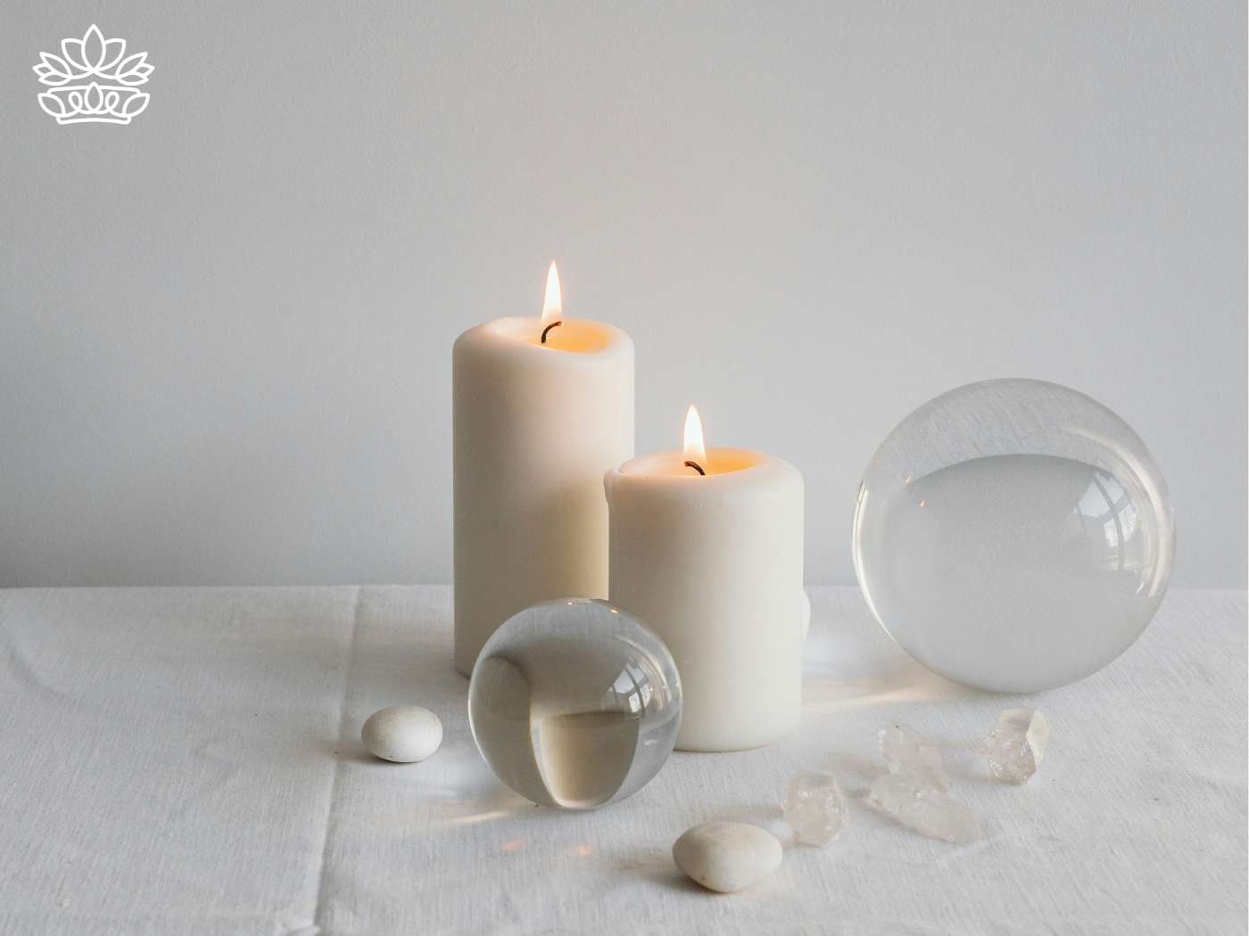 Elegant display of lit pillar candles with crystal accents and smooth pebbles on a serene white backdrop, enhancing a peaceful ambiance in the Candles Collection - Fabulous Flowers and Gifts.
