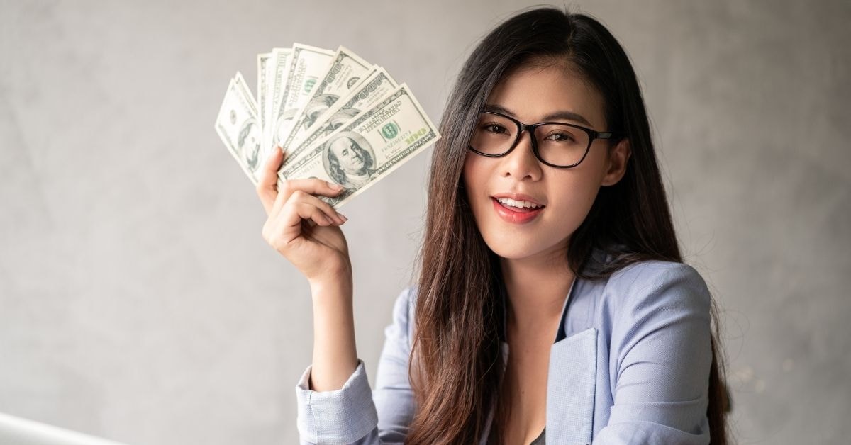 Smiling woman holding a fan of cash, representing financial success and the benefits of using a bonus tax estimator for maximizing earnings.