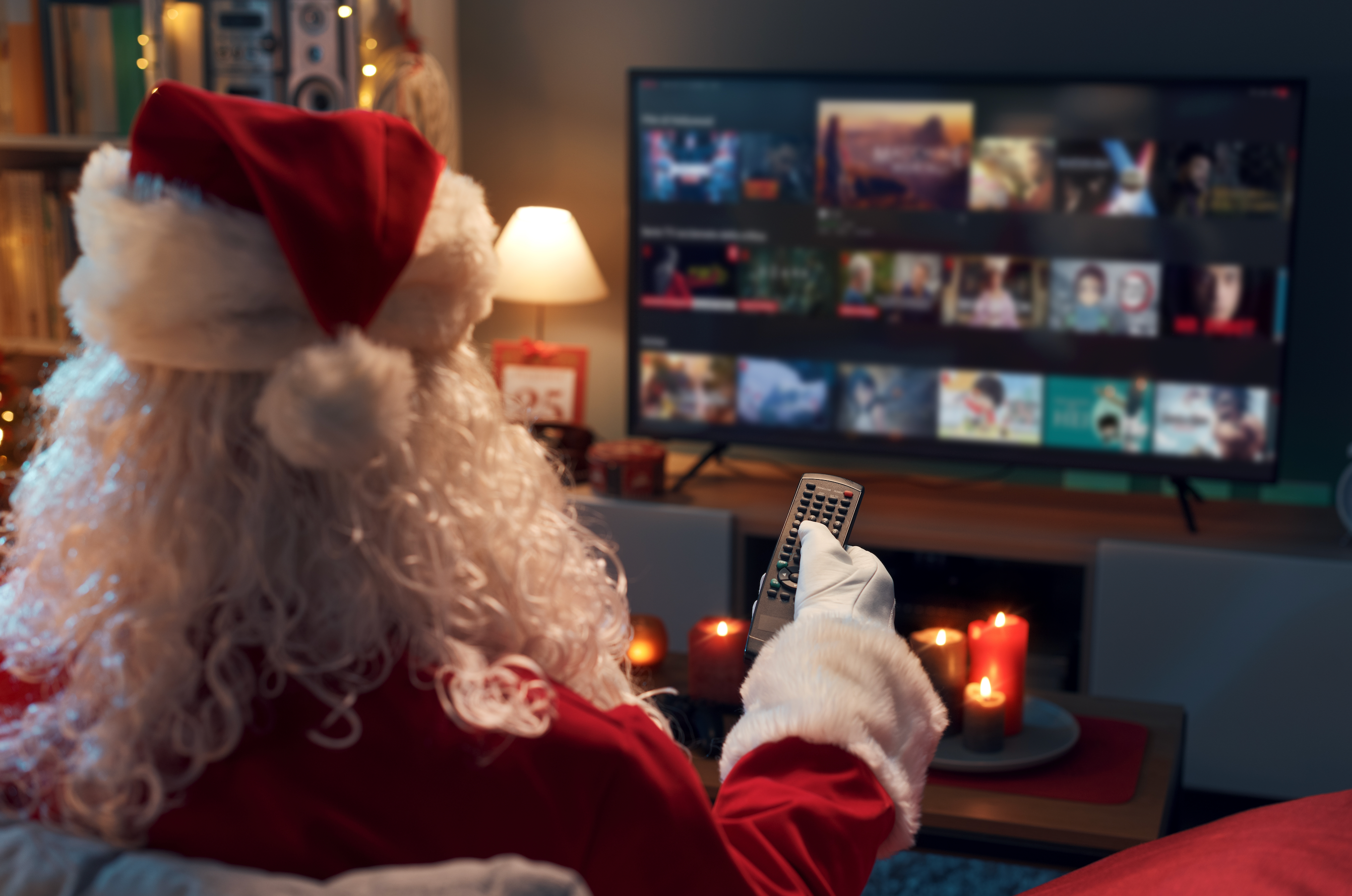 santa claus holds a tv remote and browses through streaming options while sitting on the living room couch