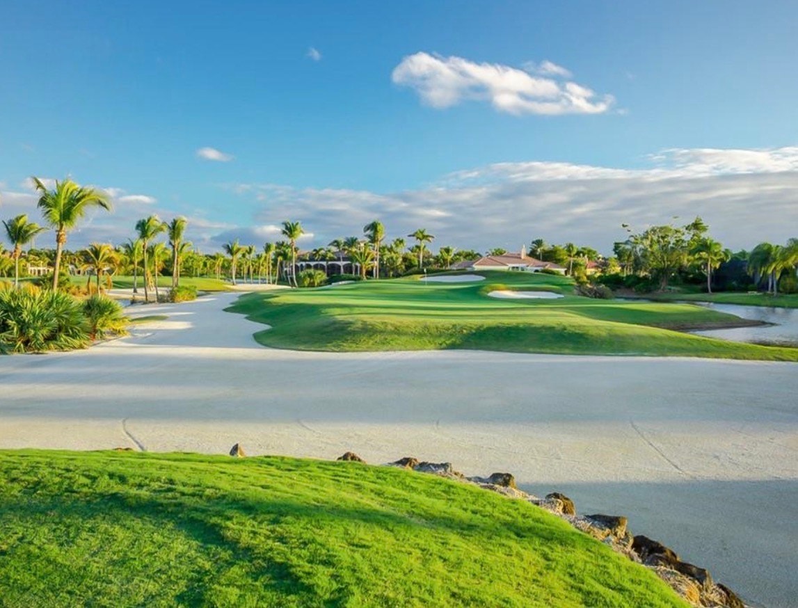 The image showcases an elegant clubhouse with Mediterranean architecture, surrounded by lush palm trees and meticulously landscaped grounds, embodying the luxurious lifestyle of Grey Oaks Naples. This magnificent property serves as a central hub for the community, offering access to resort-style amenities and championship golf courses.