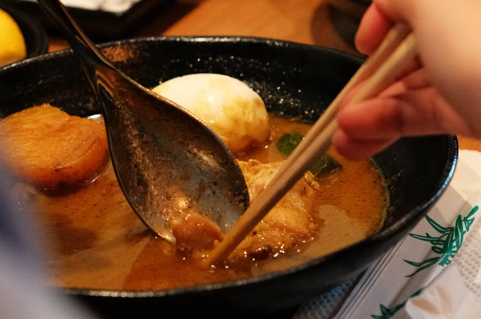 A person using chopsticks to eat from a bowl of ramen with slices of pork and an egg.