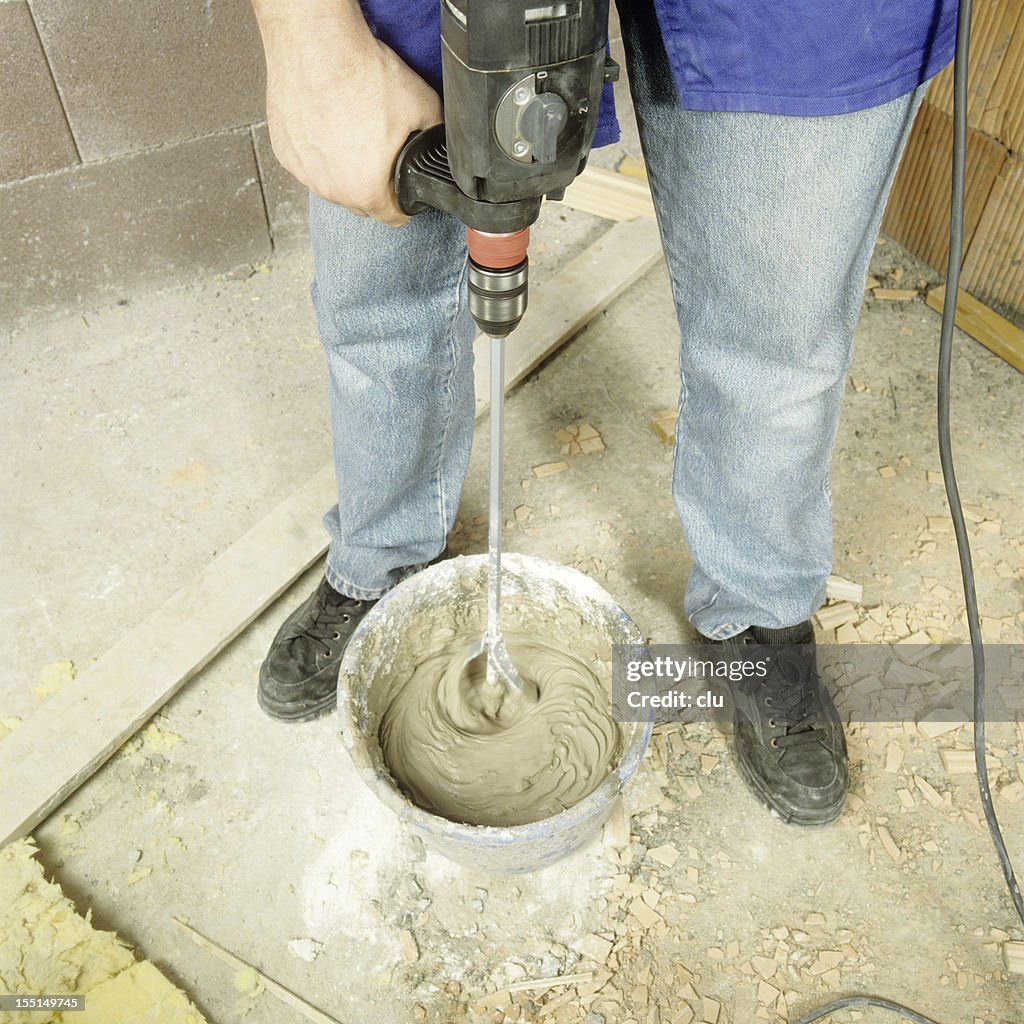 A person using a concrete mixer drill to mix cement