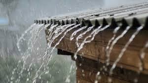 A close-up picture of rain falling off the side of a metal roof.