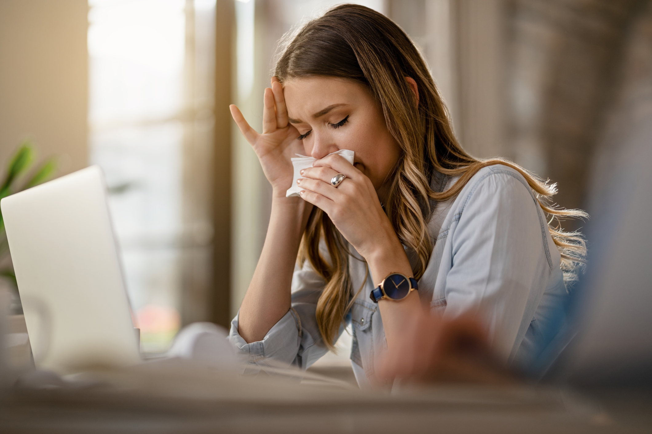 An image of a woman with postnasal drip wiping her nose with a tissue.